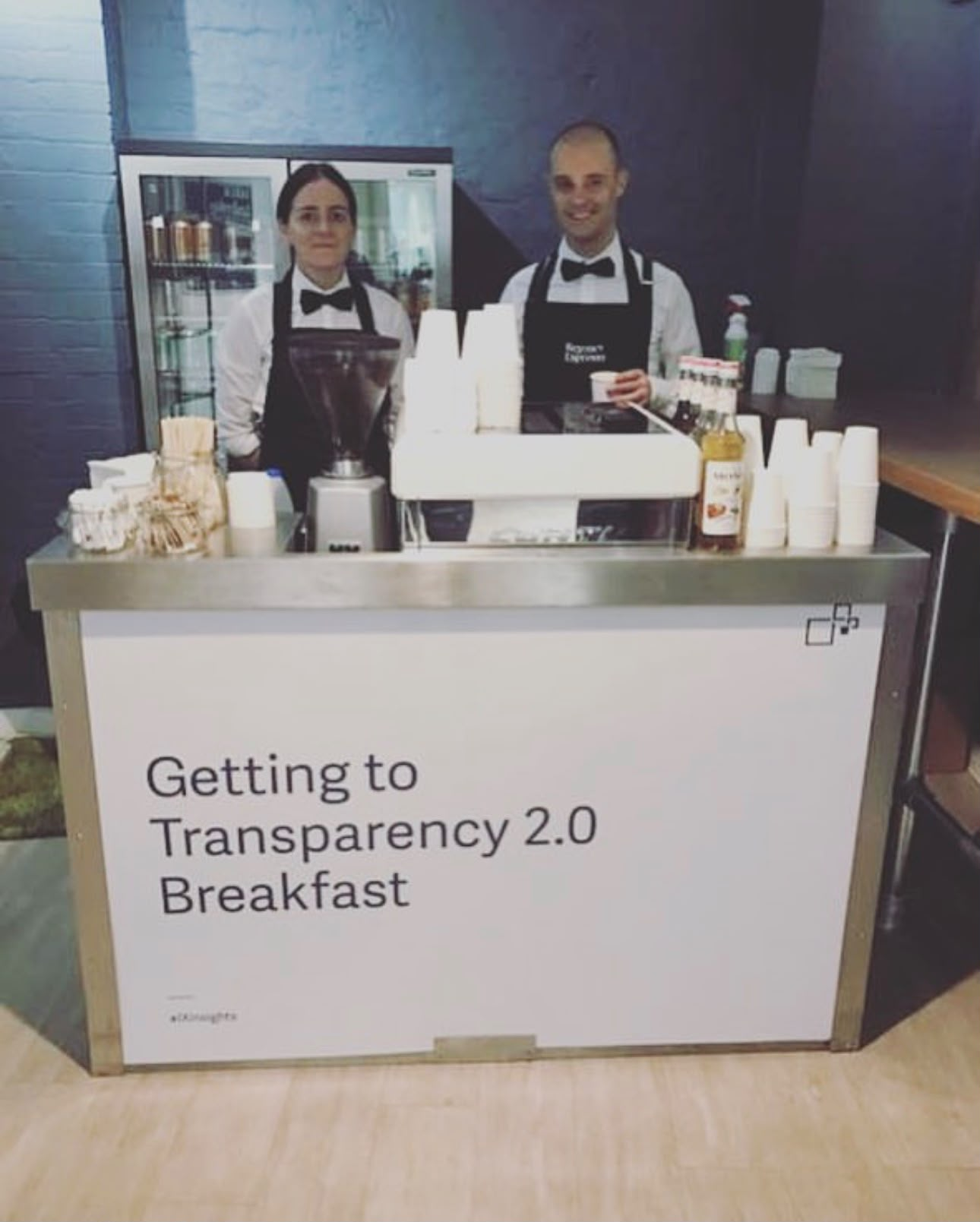 Two baristas behind a branded mobile coffee bar at a corporate breakfast event